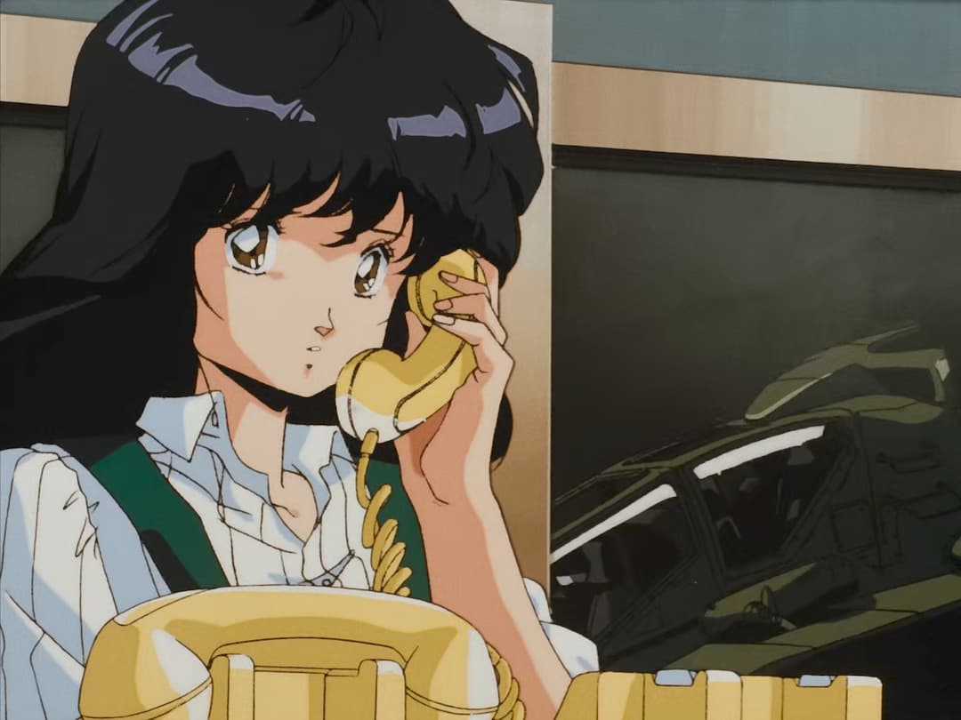 Anime character with black hair and brown eyes talking on a yellow rotary telephone while wearing a white shirt with green tie.