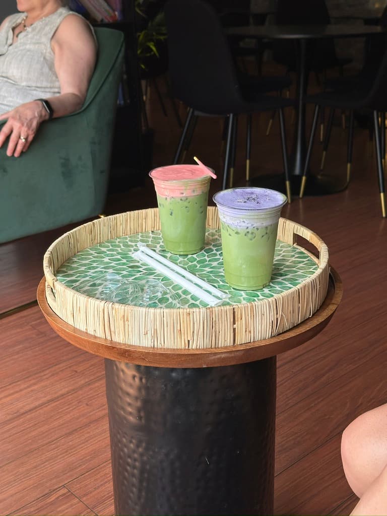 Two iced matcha drinks with pink and purple foam on a mosaic tray on a small café table.