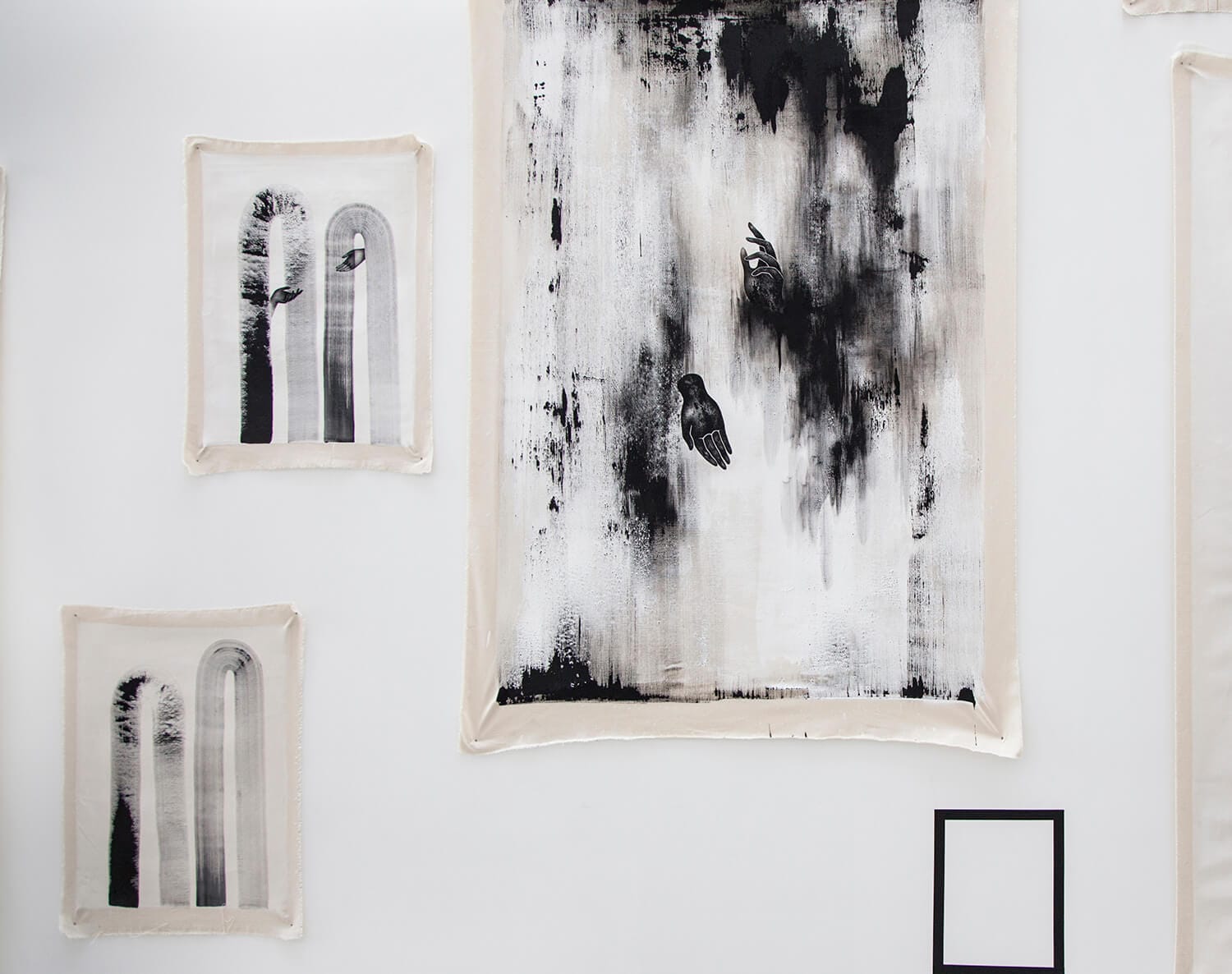 Three framed artworks on a white wall featuring black and white abstract compositions with vertical forms and bird silhouettes, alongside a small black-framed piece in the lower right corner.