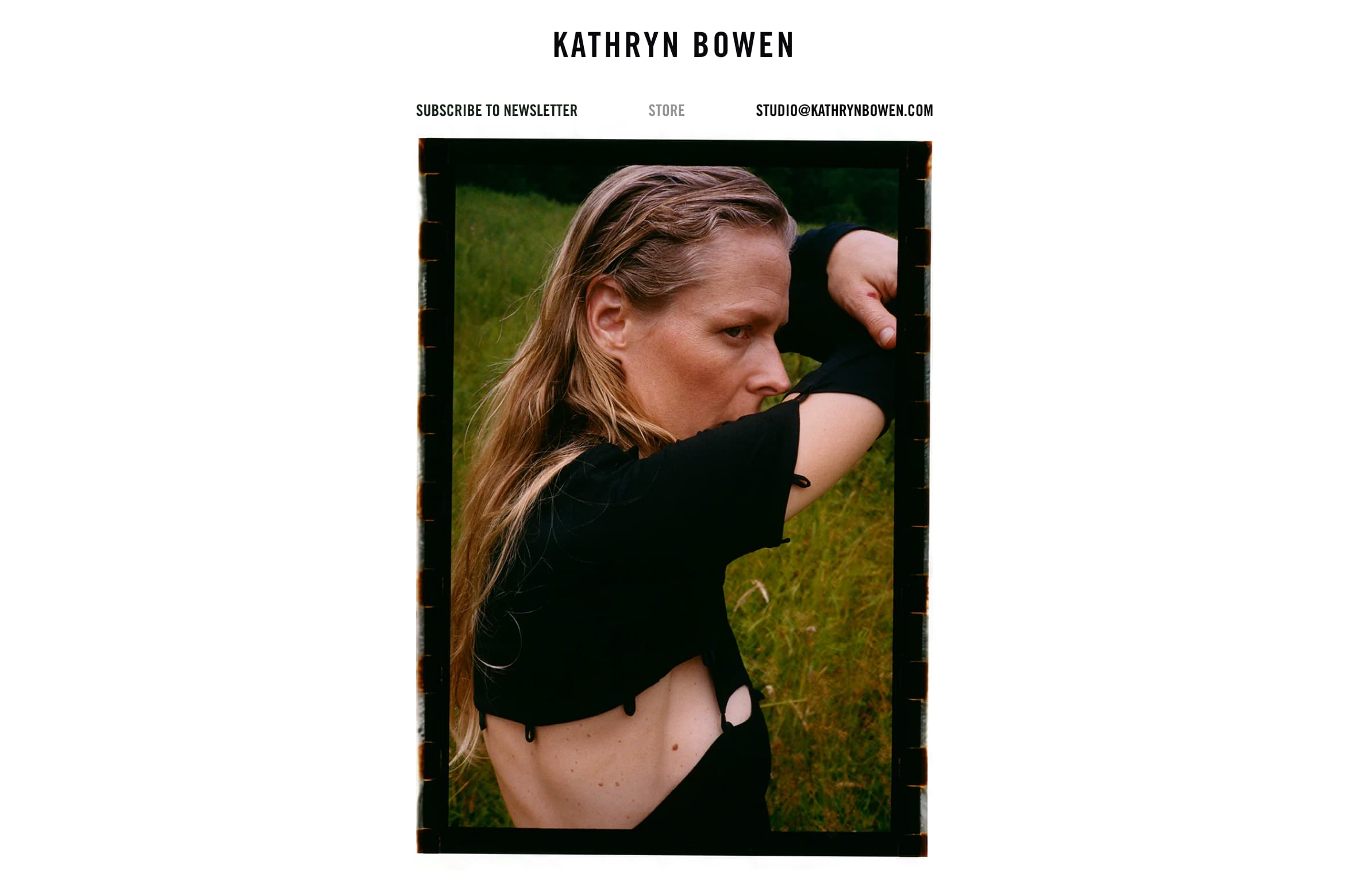 Homepage screenshot of kathrynbowen.com, featuring a person with long blonde hair posing outdoors in a black cutout top, one arm raised to partially cover their face.