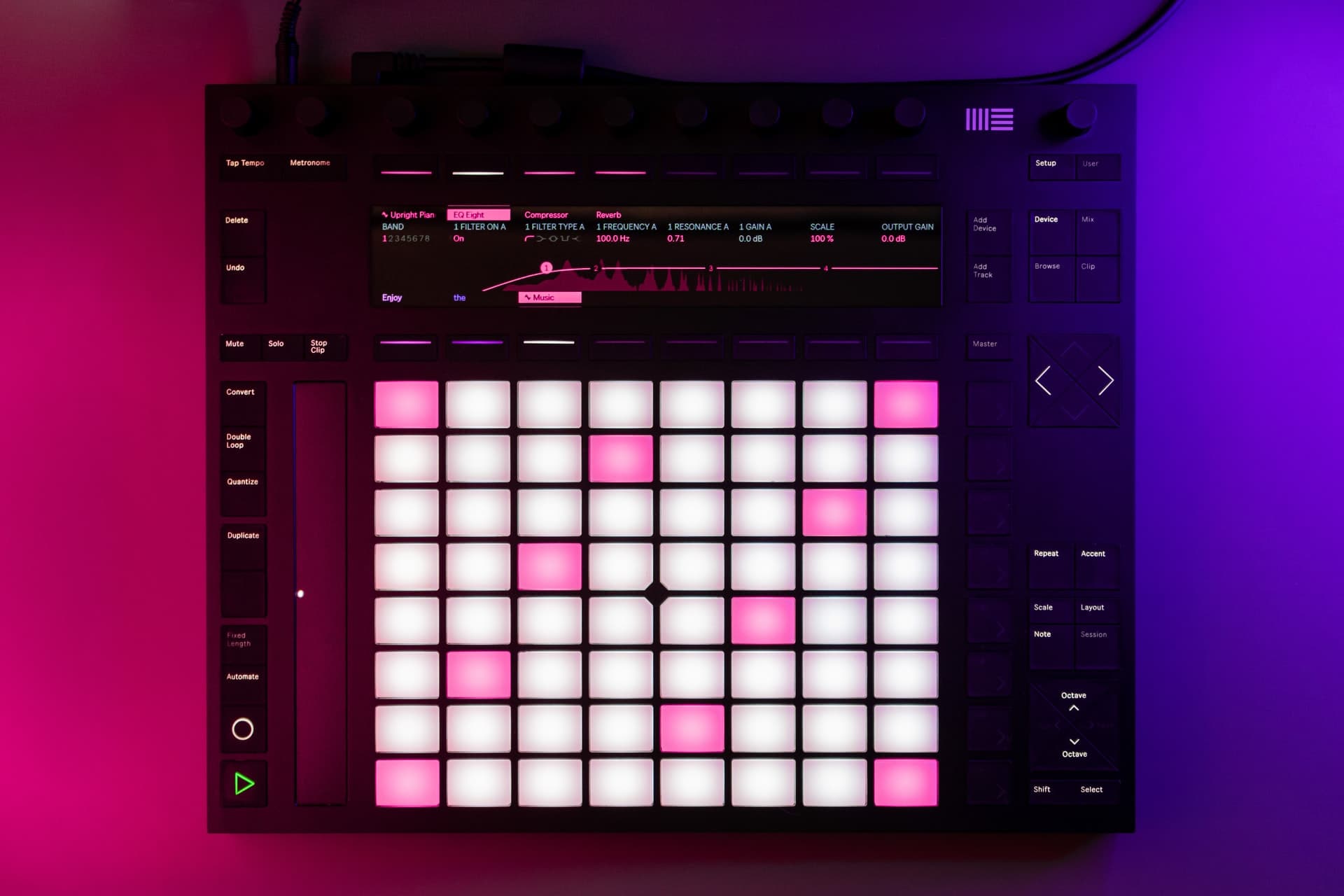 Digital music production controller with illuminated pink and white grid pads, audio effects interface, and mixing controls in purple lighting environment.